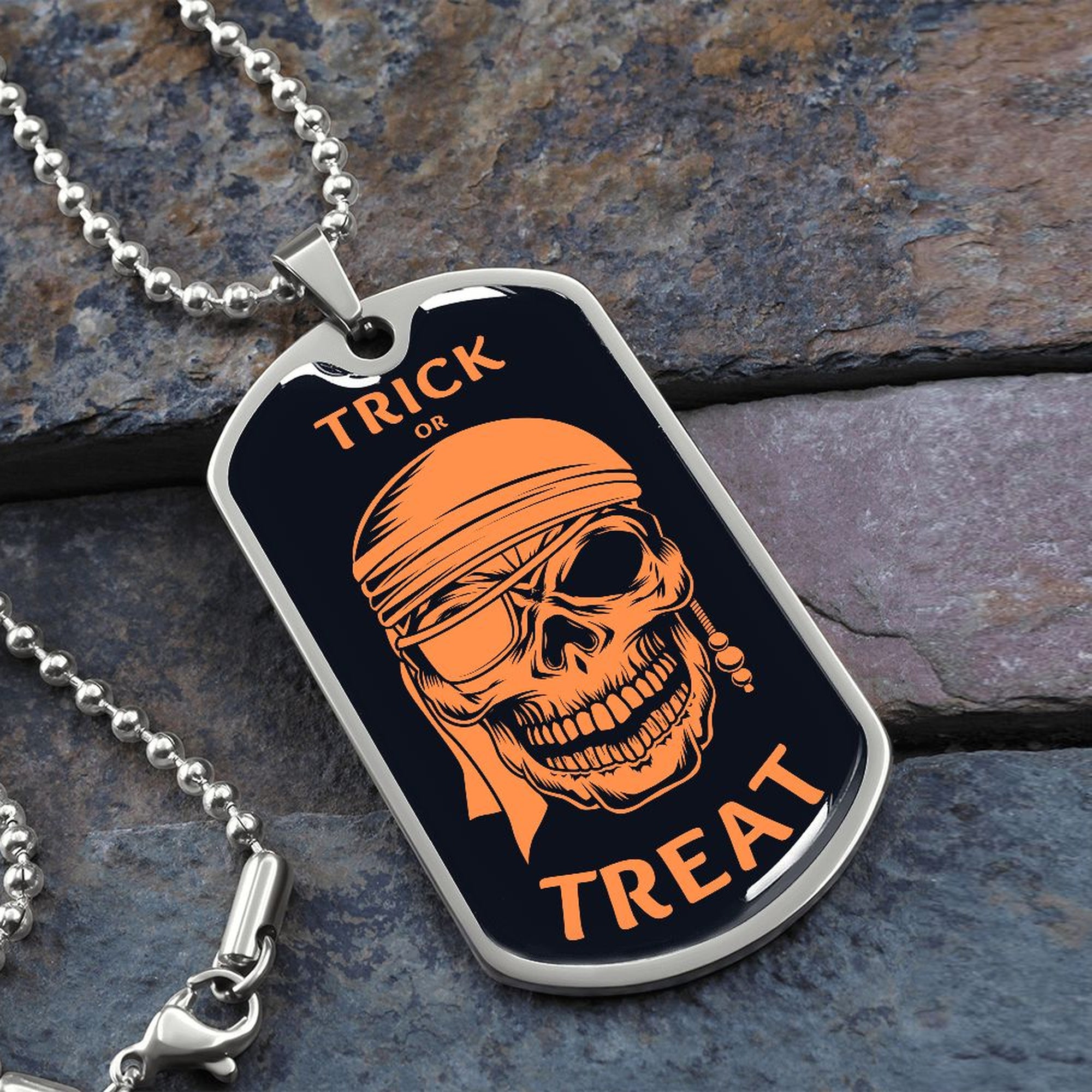 Trick or Treat pirate skull dog tag necklace in silver on a ball chain, resting on slate stone