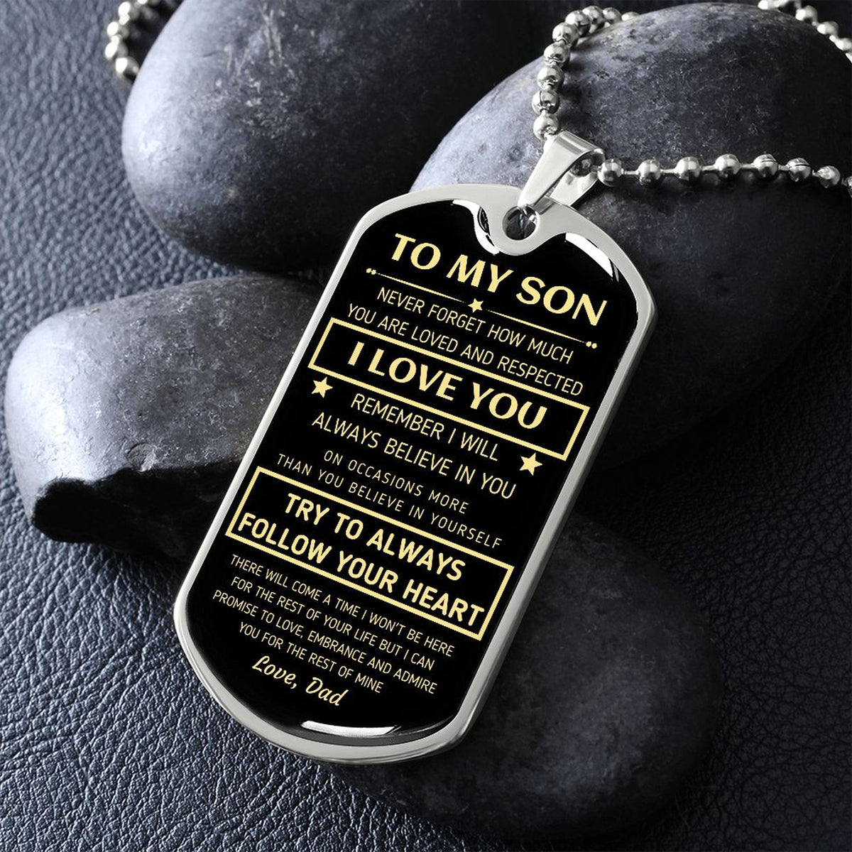 Silver To My Son dog tag propped on dark river rocks