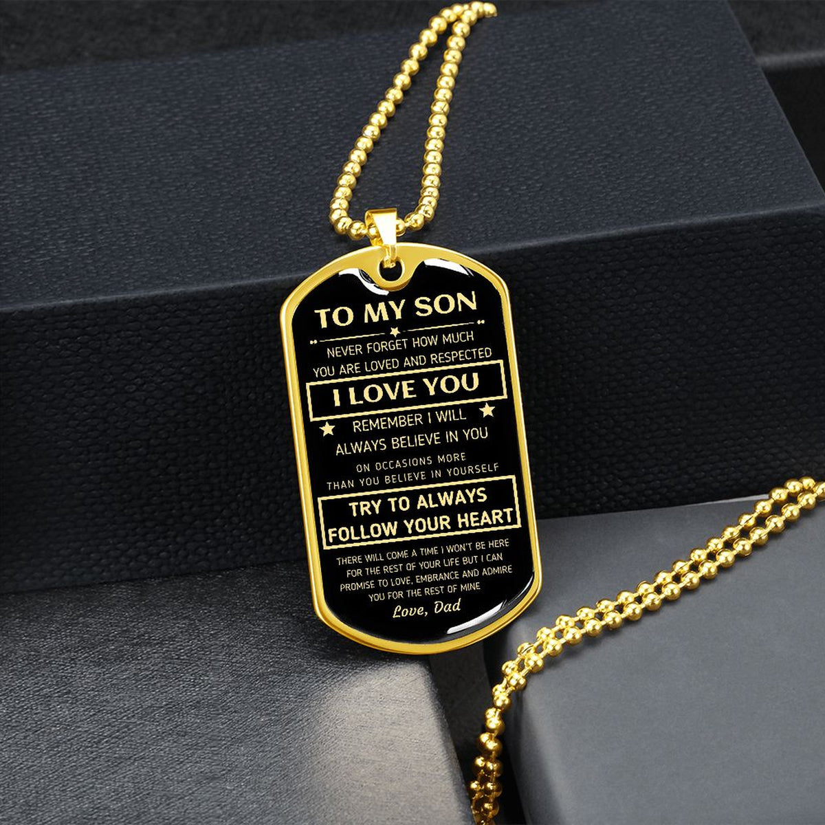 Gold-finish To My Son dog tag propped on dark river rocks